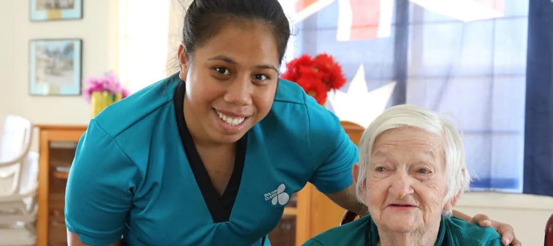 An aged-care worker smiling alongside an elderly resident.