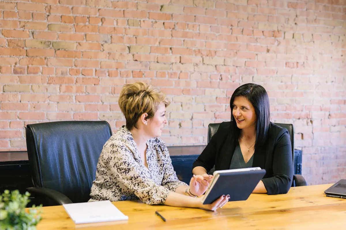 Two professionals in conversation at a meeting table.